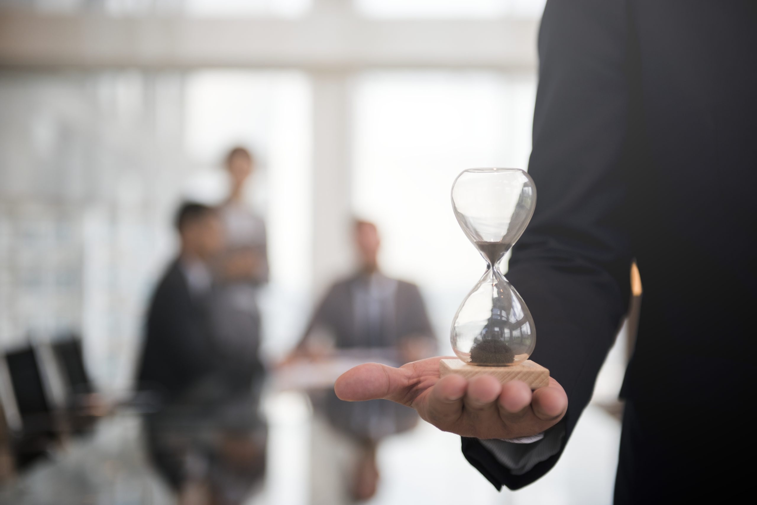 Ein Geschäftsmann hält ein Stundenglas in der Hand, um die Wichtigkeit der Pünktlichkeit zu verdeutlichen.