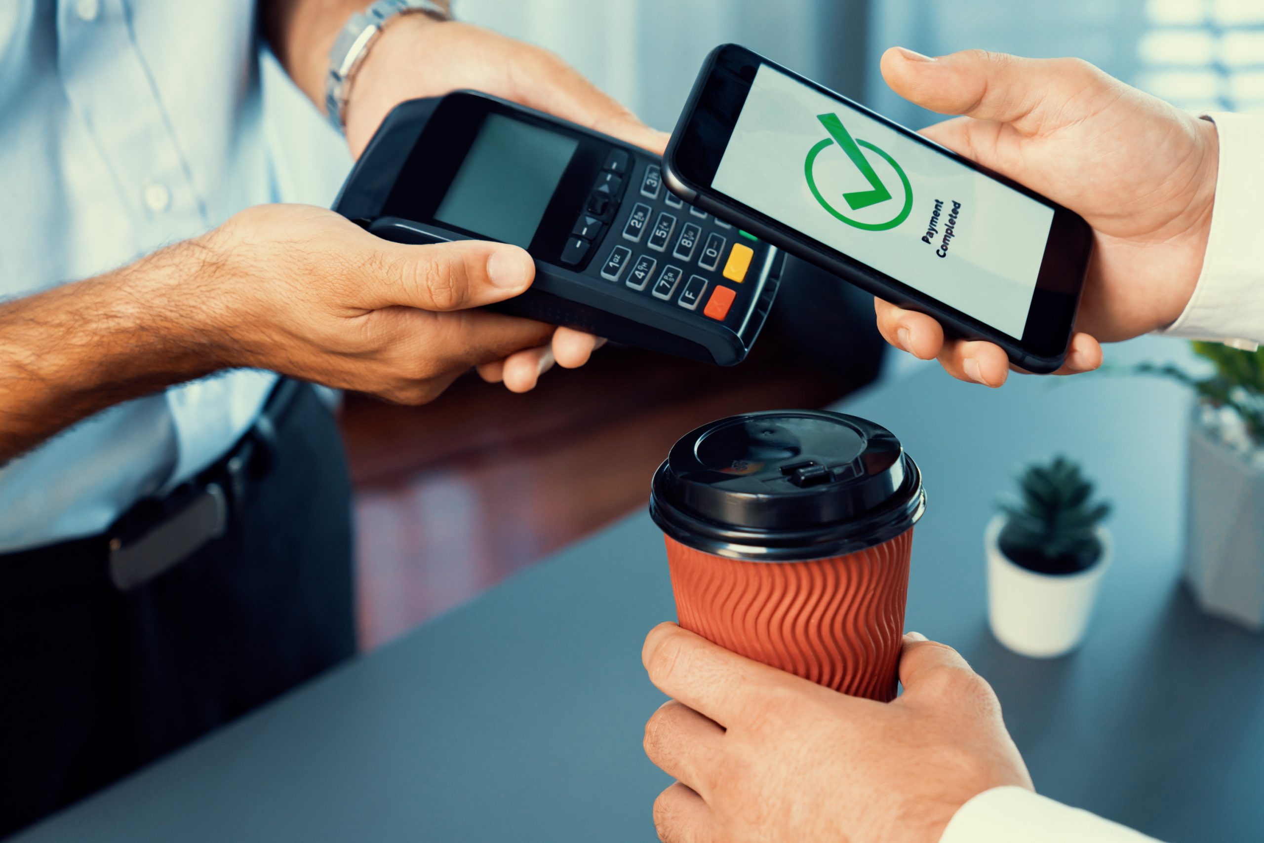 eine person nutzt ein smartphone um mit einer kaffeetasse zu bezahlen