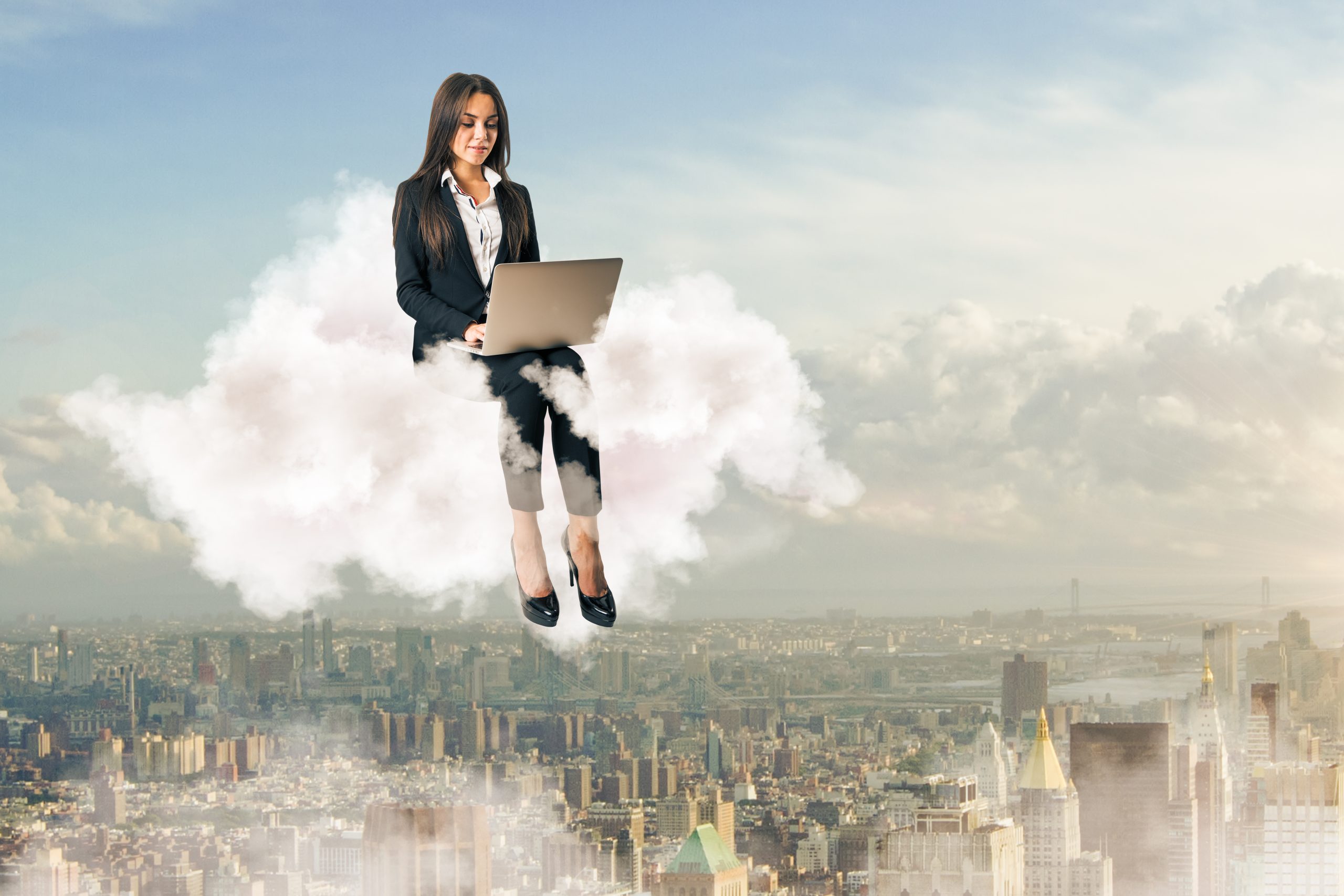 Attraktive junge europäische Geschäftsfrau, die einen Laptop benutzt, während sie auf einer Wolke auf dem Hintergrund einer Himmelsstadt sitzt. Freelance-Konzept